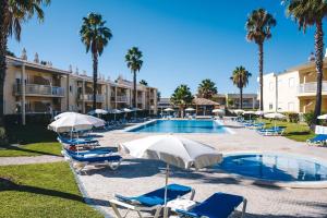 a swimming pool with chairs and umbrellas and palm trees at 1A The Apartment in Albufeira