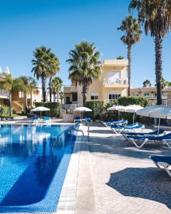 a swimming pool with chairs and umbrellas and palm trees at 1A The Apartment in Albufeira
