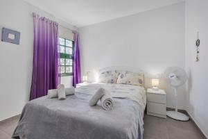 a bedroom with a bed with purple curtains and a fan at Heiwa Apartment With Pool in Costa Calma +16 photos