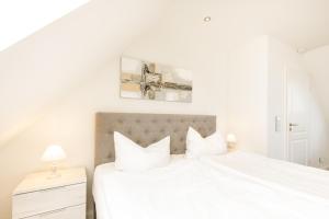 a white bedroom with a large bed with white pillows at Himmelreich in Westerland