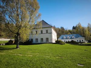 a large white house with a tree in a field at Zámeček Bischofstein in Teplice nad Metují