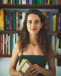 a woman holding a book in front of a book shelf at Island Diaries Hostel in Katunayaka