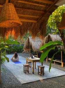 a woman sitting on a rug under a hut with a table and benches at Island Diaries Hostel in Katunayaka