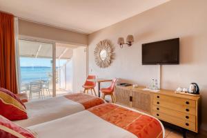 a hotel room with two beds and a television at Roc Hotel - Hôtel 4 étoiles les pieds dans l'eau in Le Lavandou