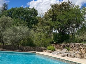 a swimming pool with two lounge chairs next to a stone wall at Le Verger in Gordes