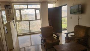 a living room with two chairs and a table and windows at ONHILLs in Mussoorie