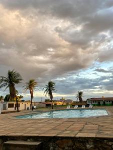 a swimming pool with palm trees and a cloudy sky at Carranca Grande Hotel in Xique-Xique