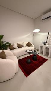 a white living room with a white couch and a red rug at AURA Stay in Dammam