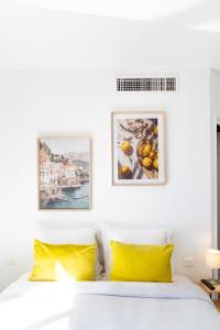 a white bedroom with yellow pillows and pictures on the wall at Hôtel la Rotonde in La Croix-Valmer