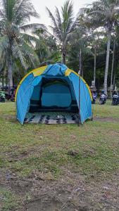 a blue and yellow tent in a field with palm trees at Tenda Premium Pantai Madasari in Bulakbenda
