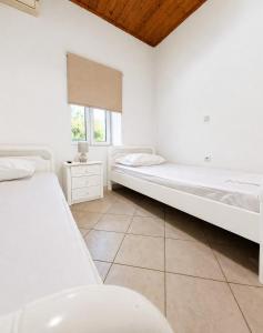 two beds in a white room with a window at Nature's Nook Paxos in Vlachopoulátika