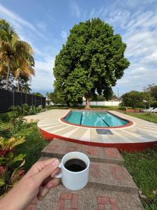 a person holding a cup of coffee next to a pool at Casona El Remanso in Mariquita