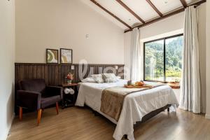 a bedroom with a bed and a chair and a window at Faxinal das Águas Retreat - 5min from downtown in Rancho Queimado