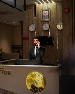 a man standing at a counter talking on a cell phone at Wan Hotel in Duhok