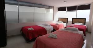 three beds in a room with red sheets at Hotel the Blue House in Ipiales