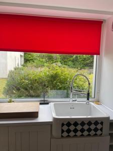 a kitchen window with a red curtain over a sink at Le Clos - Proximité plage in Ambleteuse +20 photos