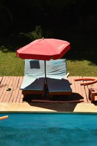 a red umbrella and chairs next to a swimming pool at Rincón de Rodríguez in General Rodríguez