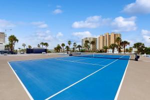 a blue tennis court with palm trees and buildings at Broadmoor 604 in Orange Beach