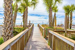 a wooden boardwalk with palm trees and the ocean at Regency Isle 611 in Orange Beach