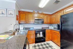 a kitchen with wooden cabinets and a black refrigerator at Perfectly located condo with beach access - deck internet W&D & AC in Dauphin Island +9 photos