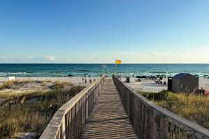 a wooden boardwalk to the beach with a yellow flag at Spacious beachfront condo with full kitchen shared pool and beach access in Gulf Shores