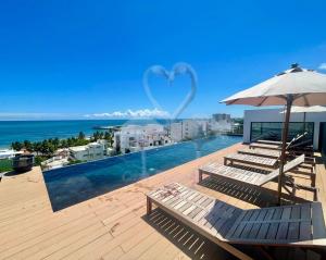a swimming pool with chairs and an umbrella and the ocean at Private Suite, Walk to the Beach, Oceanview Rooftop Pool, WiFi StarLink in Puerto Morelos