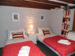 2 Betten in einem Schlafzimmer mit roter und weißer Bettwäsche in der Unterkunft Primrose Cottage in North Petherwin
