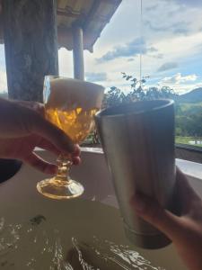 a person holding a glass of beer and a cup at Chalé Água Santa in São Thomé das Letras