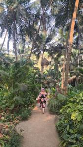 a woman walking down a path in a garden with palm trees at Laxmi Happy Home in Querim Goa in Querim