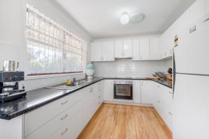 a kitchen with white cabinets and a wooden floor at Mirrabooka in Lake Cathie