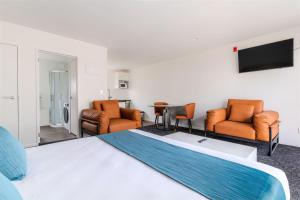 a hotel room with a bed and chairs and a flat screen tv at Te Awa Suites in Hamilton