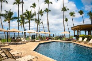 a pool with chairs and umbrellas and palm trees at Mana Kai Maui Condo - Right on the Beach! in Wailea