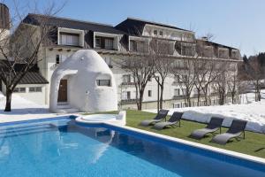 a swimming pool with two chairs and a building at The Alps Hotel Hakuba in Otari