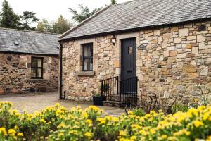 a stone building with a black door and some flowers at Blueberry Cottage in Wooler