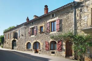 a stone building with red shutters on a street at Maison des papillons Daglan in Daglan