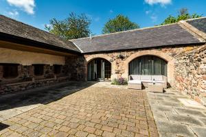 an old stone building with a bench in the courtyard at Lupin Cottage in Wooler