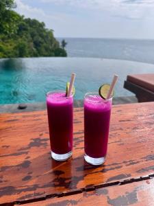 two glasses of pink juice sitting on a wooden table at Makawi Tuwa Cliff - Luxury Cliff Stay with Private Beach, Infinity Pools and Ocean View in Seraya