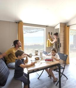 a family sitting at a table in a living room at Camping 3 étoiles - 1km de la plage - Piscine chauffée et Espace Fitness in Saint-Georges-de-Didonne