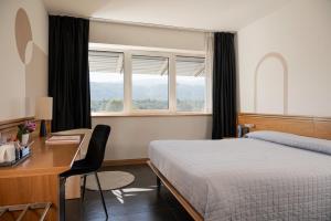 a hotel room with a bed and a desk and windows at Hotel Europa Belluno in Belluno