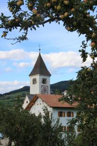 ein weißes Gebäude mit einem Uhrturm mit Bäumen in der Unterkunft Planitzhof in Kastelruth