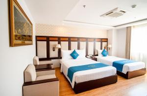 a hotel room with two beds and a chair at Galliot Hotel Nha Trang in Nha Trang