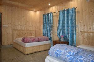 two beds in a room with wooden walls and blue curtains at Devdaar Cottage Gangotri in Gangotri