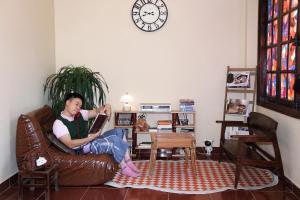 a man sitting on a leather couch reading a book at Maison MAY Đà Lạt in Da Lat