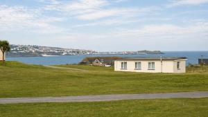 a white house on a grassy hill next to the water at F59 Trevone, Riviere Towans in Hayle
