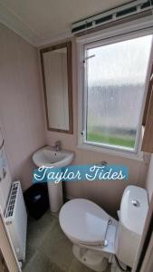 a bathroom with a toilet and a sink and a window at Taylor Tides Caravan in Abergele +8 photos
