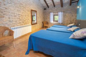 a bedroom with two blue beds and a stone wall at Can Mas in Fontcuberta