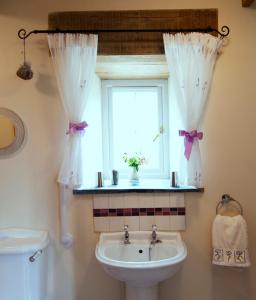 een badkamer met een wastafel en een raam met gordijnen bij The Old Wagon House in Saint Clether