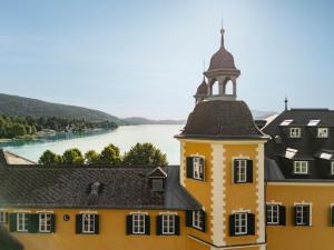 a yellow building with a tower with a river in the background at Falkensteiner Schlosshotel Velden – The Leading Hotels of the World in Velden am Wörthersee +39 photos