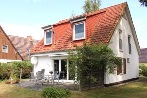 a white house with an orange roof and chairs at Ferienhaus Lütt Matten in Wustrow