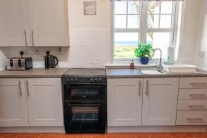 a kitchen with white cabinets and a black oven at Shell Cottage in Whithorn